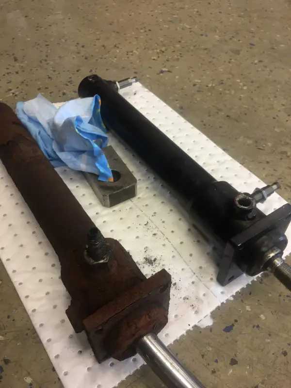 En rostig hydraulcylinder bredvid en renoverad